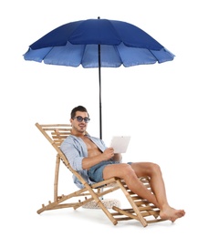 Photo of Young man with tablet on sun lounger under umbrella against white background. Beach accessories