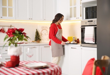 Photo of Young woman with sweet buns for Christmas dinner in kitchen