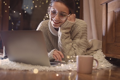 Photo of Woman with cup of hot beverage using laptop at home in winter evening