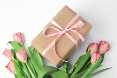 Photo of Beautiful gift box with bow and pink tulips on white background, above view