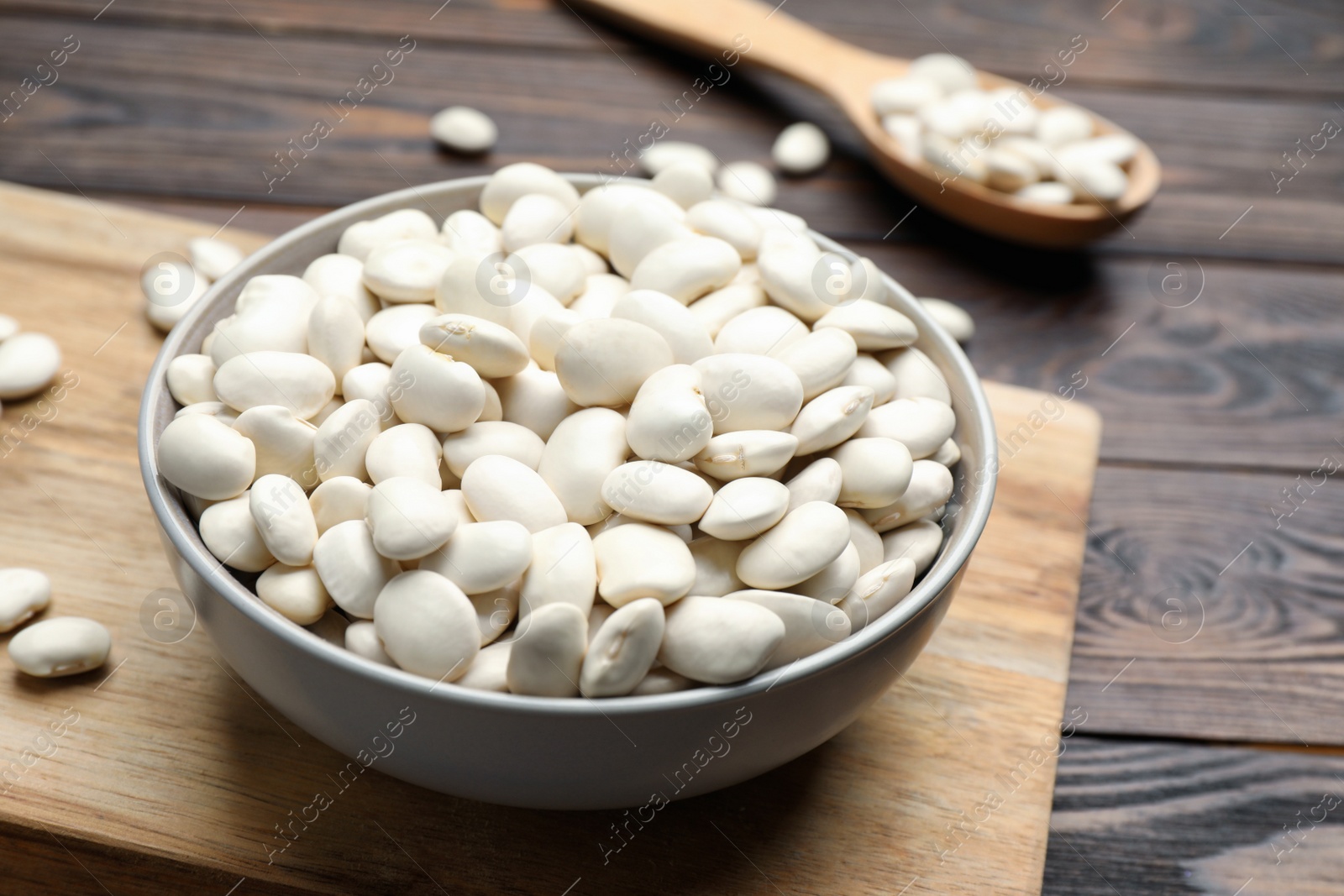 Photo of Raw white beans and bowl on wooden table, closeup