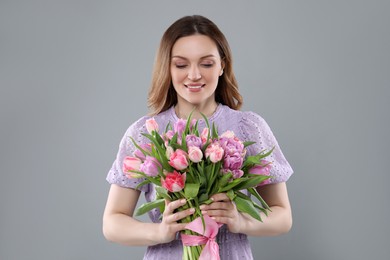 Photo of Happy young woman with bouquet of beautiful tulips on grey background