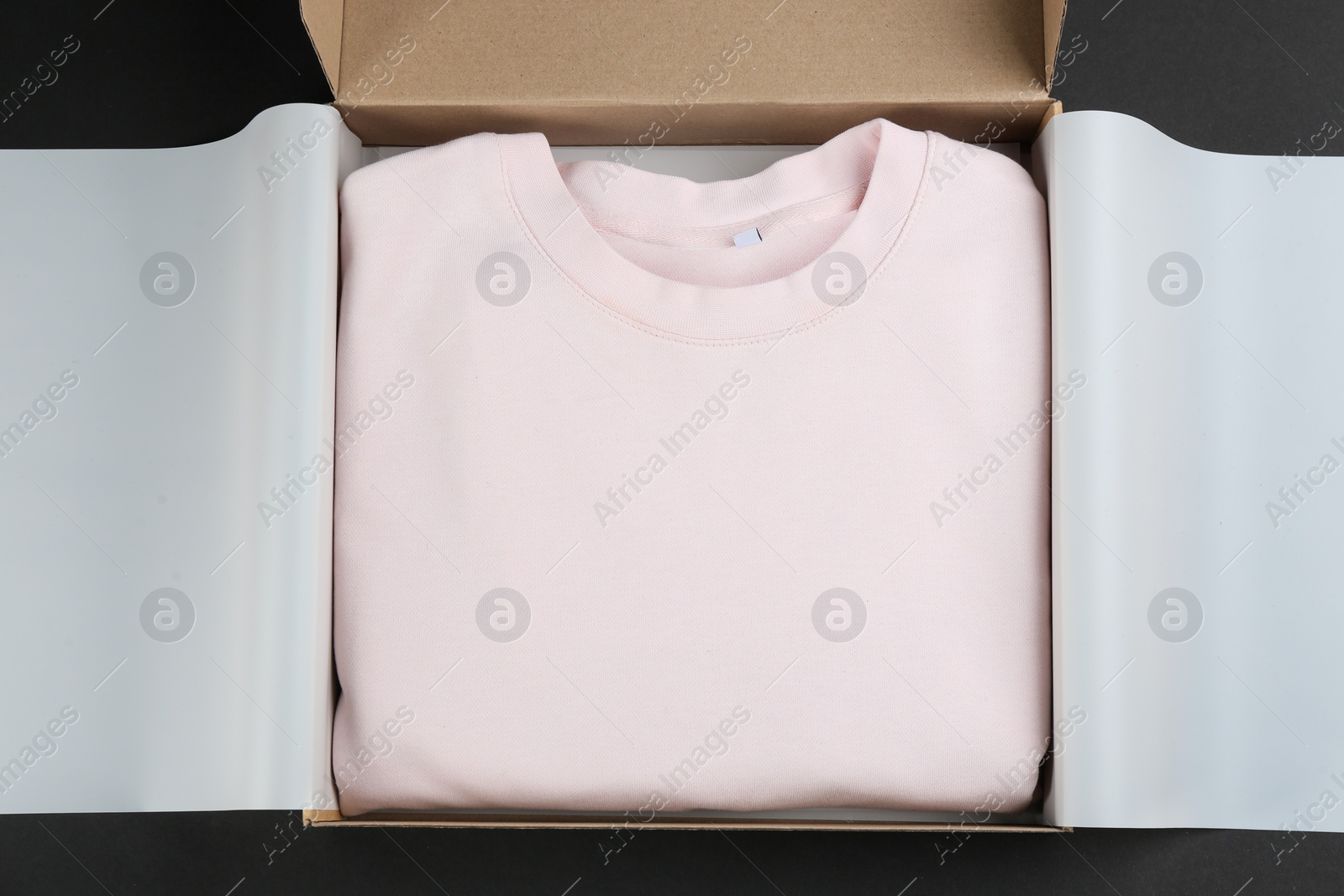 Photo of Cardboard box with clothes on black background, top view