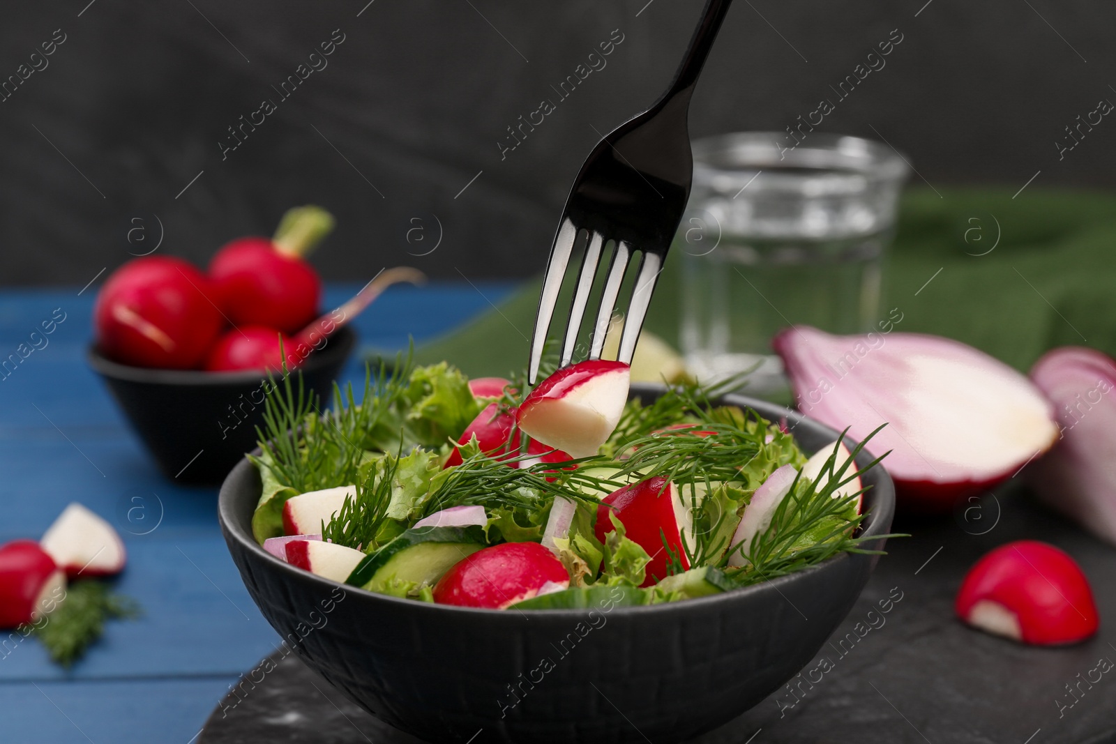 Photo of Eating salad with radish on blue table, closeup