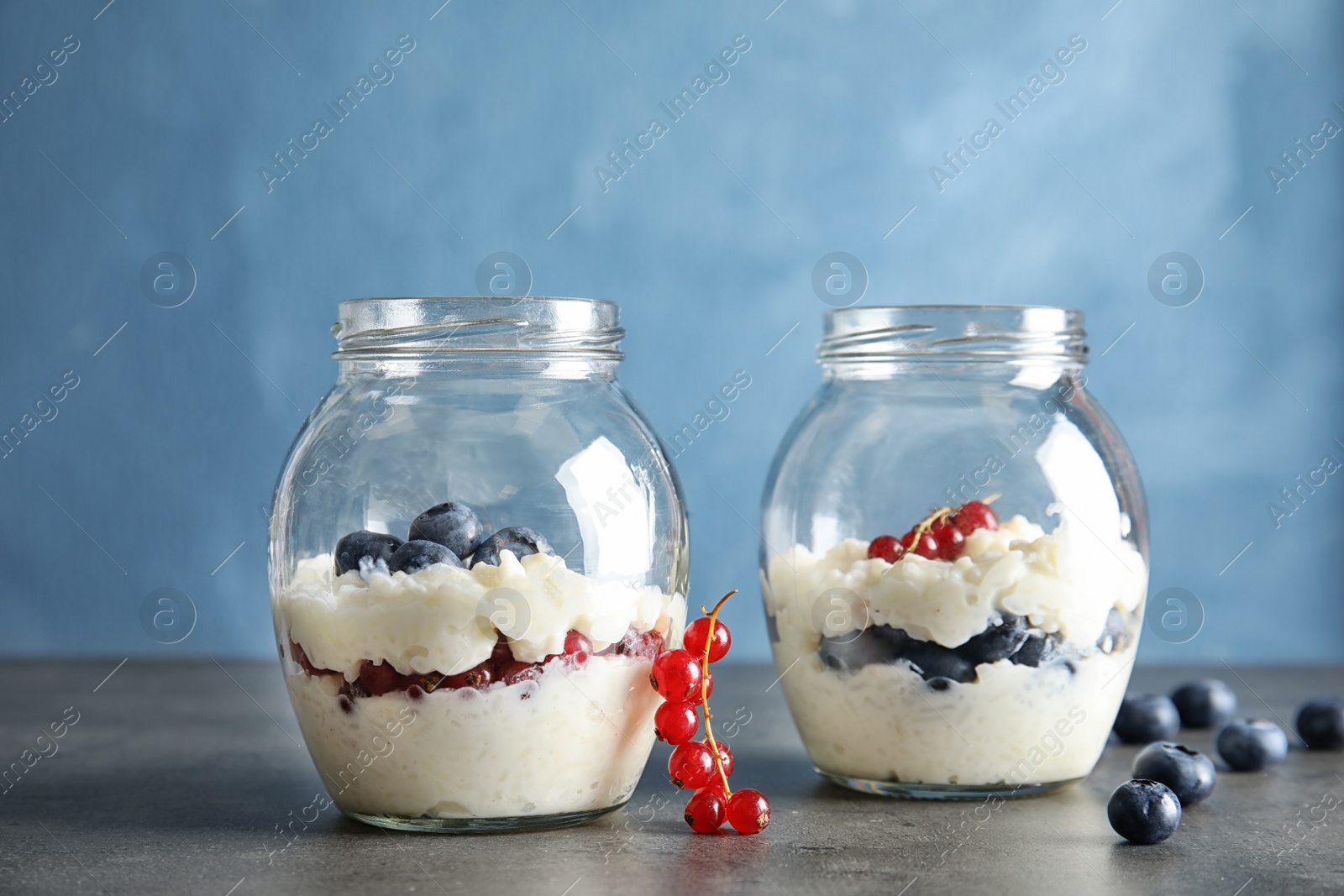 Photo of Creamy rice pudding with red currant and blueberries in jars on table