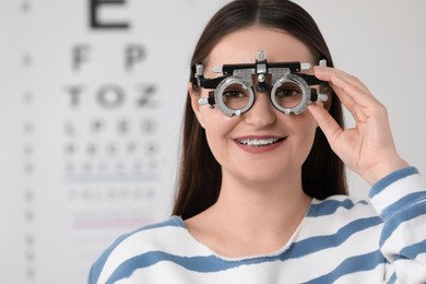 Young woman with trial frame against vision test chart