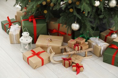 Beautifully wrapped gift boxes, wooden sleigh and lantern under Christmas tree indoors