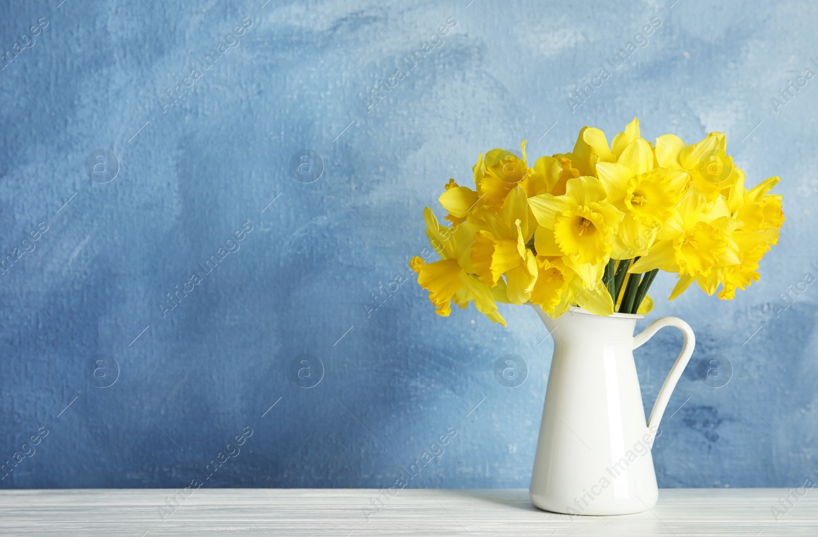 Photo of Bouquet of daffodils in jug on table against color background, space for text. Fresh spring flowers