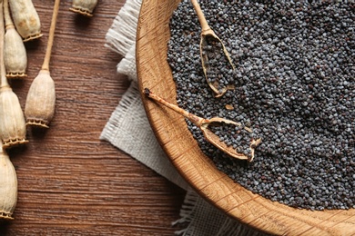 Dry poppy heads and plate with seeds on wooden background, top view