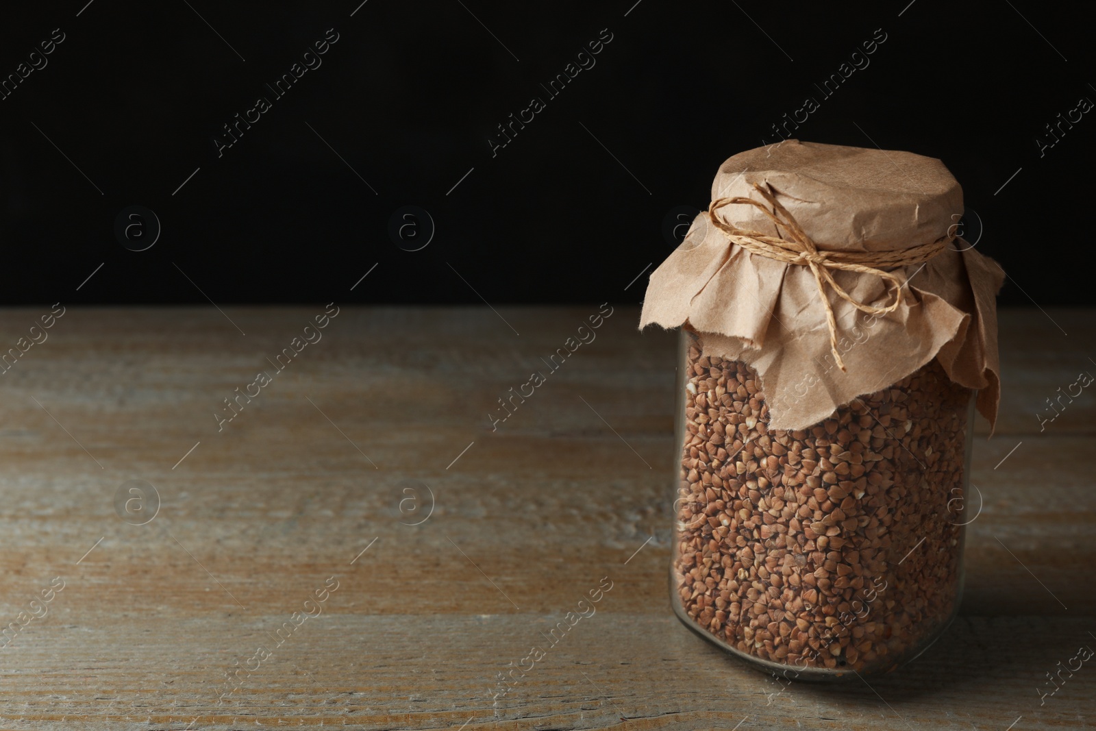 Photo of Buckwheat grains in jar on wooden table. Space for text