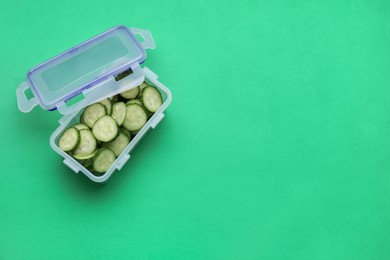 Photo of Plastic container with fresh cut cucumbers and lid on green background, above view. Space for text