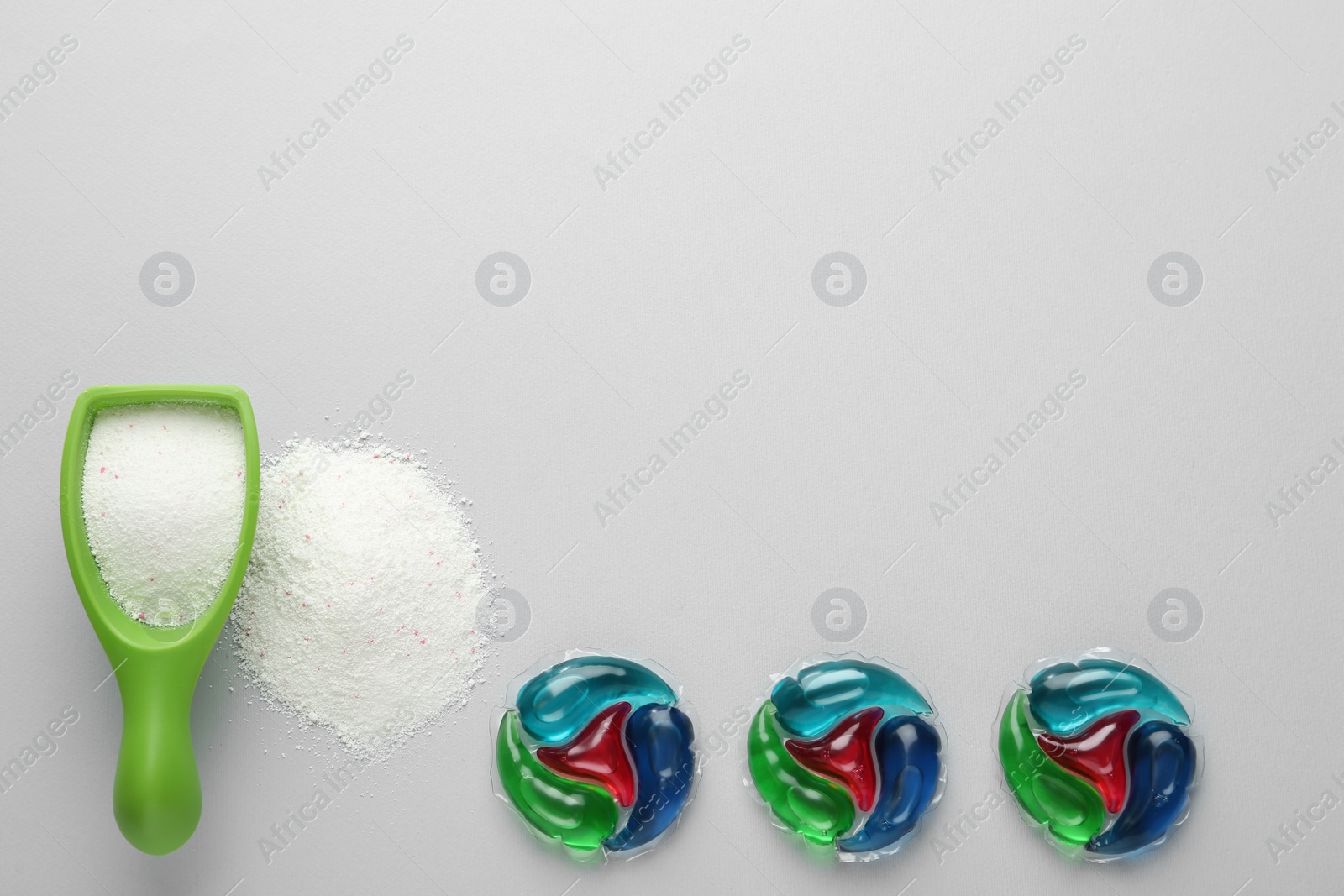 Photo of Laundry capsules and detergent powder on light grey background, flat lay. Space for text