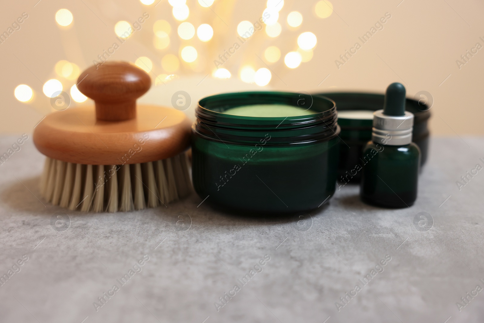 Photo of Natural scrub and other body care products on grey table against blurred lights