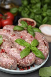 Photo of Raw homemade sausages, basil leaves and peppercorns on grey table, closeup