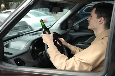 Photo of Man with bottle of beer driving car, view from outside. Don't drink and drive concept