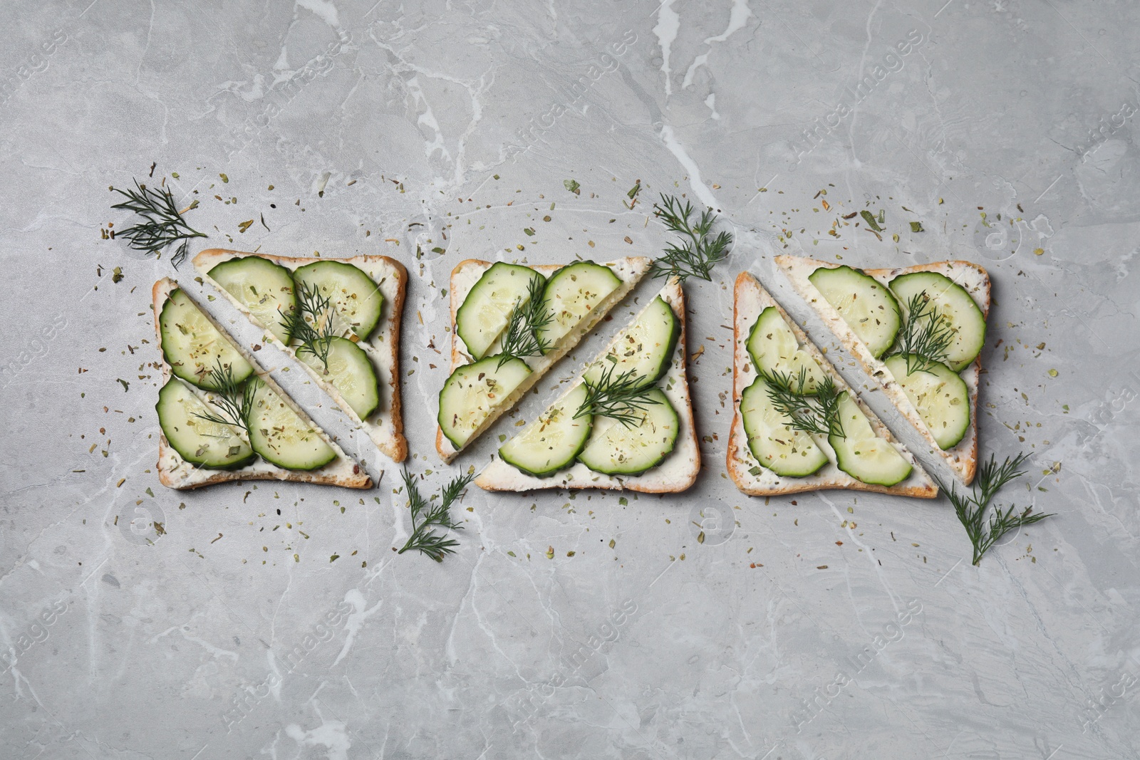 Photo of Tasty sandwiches with cream cheese, cucumber and dill on grey marble table, flat lay