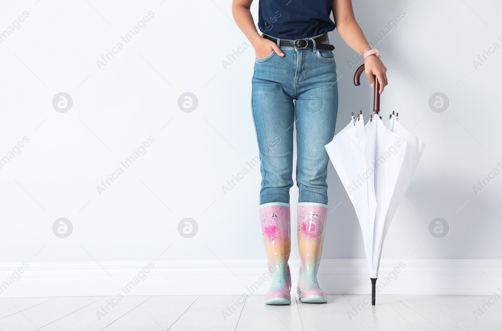 Photo of Woman in gumboots holding bright umbrella near white wall with space for design