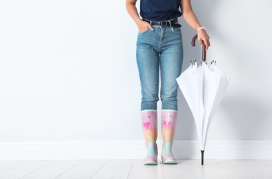 Woman in gumboots holding bright umbrella near white wall with space for design