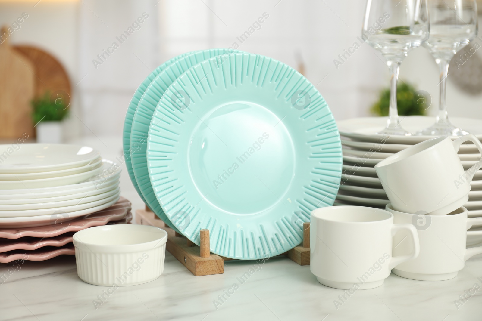 Photo of Clean plates, cups, glasses and bowl on white marble table in kitchen