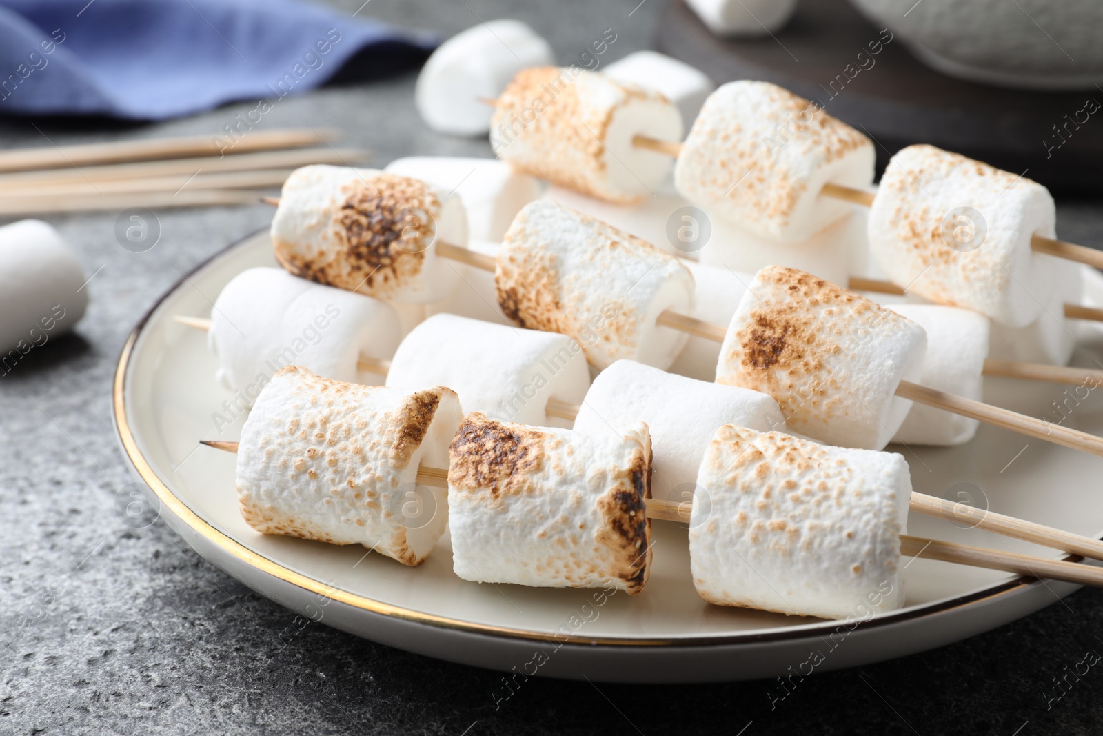Photo of Sticks with roasted marshmallows on grey table, closeup