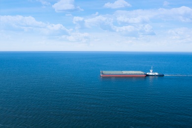 Image of Tugboat pulling barge with cargo by water, aerial view