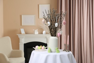 Photo of Pussy willow branches with festively decorated eggs, Easter bunnies and candles on table indoors