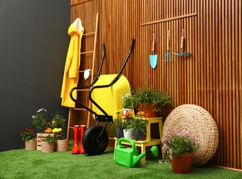 Gardening tools with wheelbarrow and flowers near wooden wall