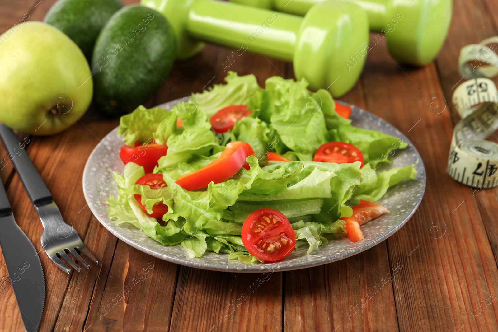 Photo of Healthy diet. Salad, cutlery, dumbbells and measuring tape on wooden table, closeup