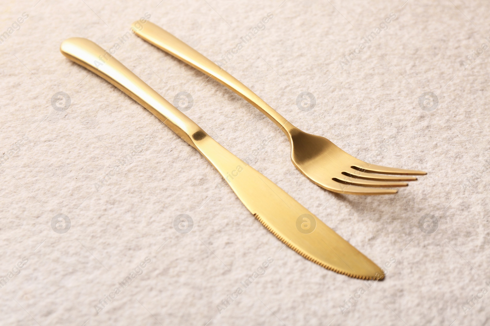 Photo of Stylish cutlery. Golden knife and fork on light textured table