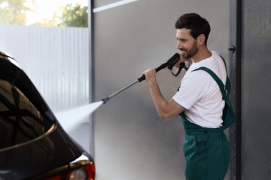 Worker washing auto with high pressure water jet at outdoor car wash