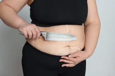 Obese woman with knife and marks on body against light background, closeup. Weight loss surgery