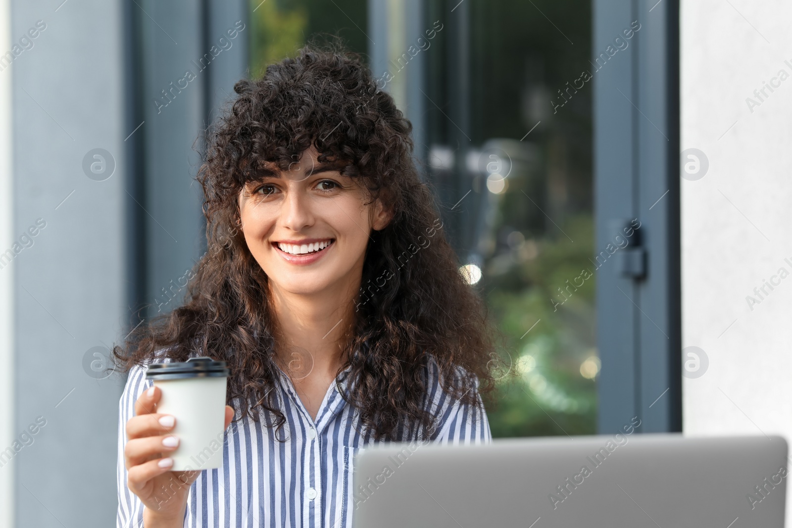 Photo of Happy young woman with cup of coffee using modern laptop outdoors