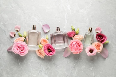 Flat lay composition of different perfume bottles and flowers on light grey marble background