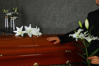 Photo of Young man with white lilies near casket in funeral home, closeup