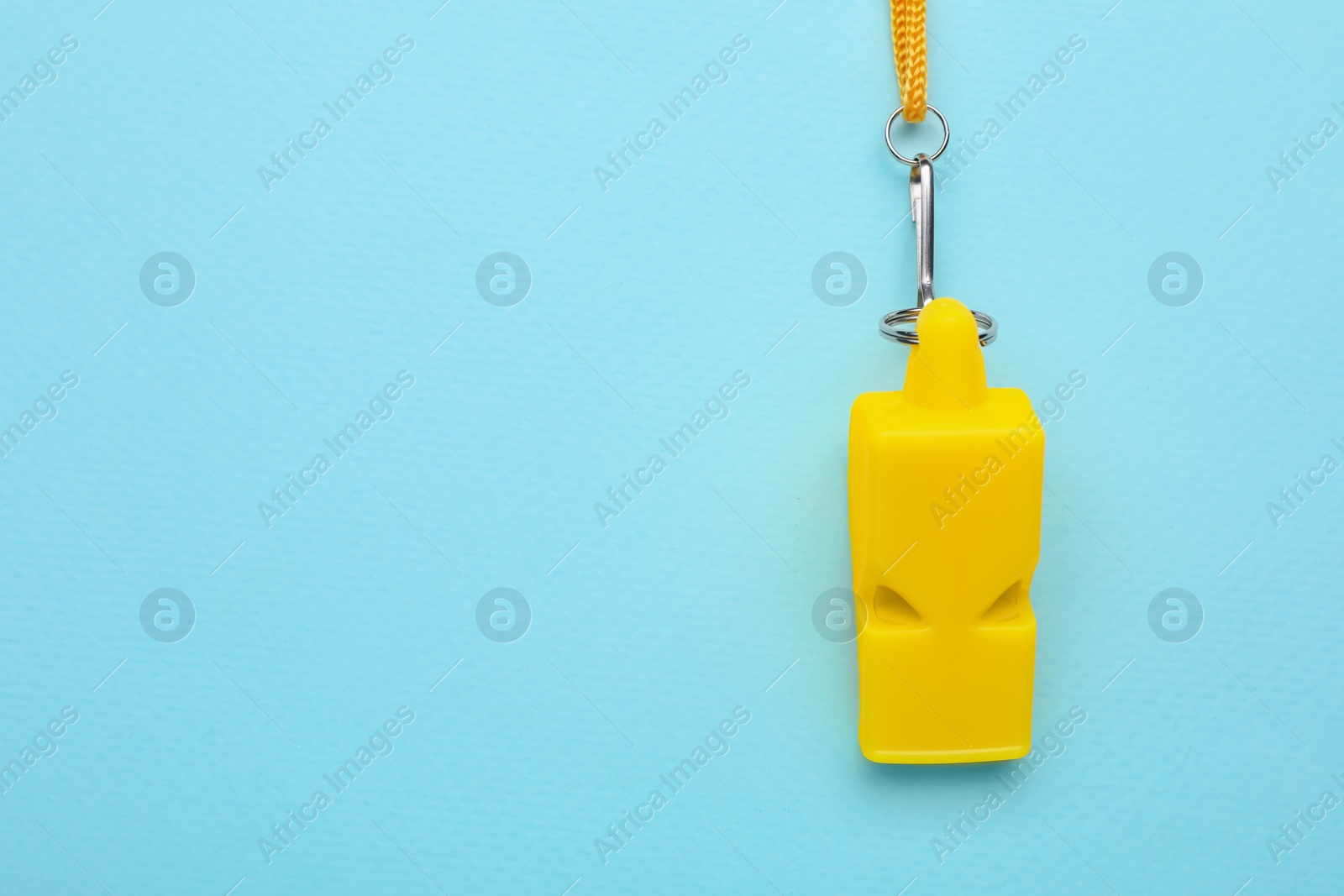Photo of One yellow whistle with cord on light blue background, top view. Space for text