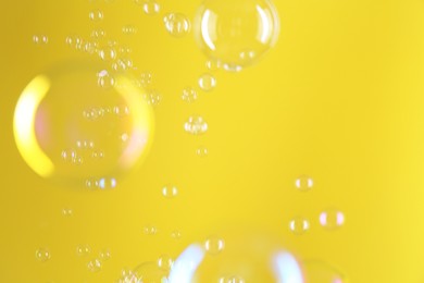 Photo of Beautiful transparent soap bubbles on yellow background