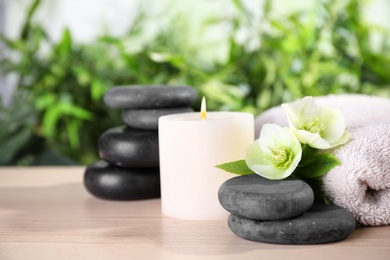 Photo of Composition with spa stones, towel and candle on wooden table, space for text