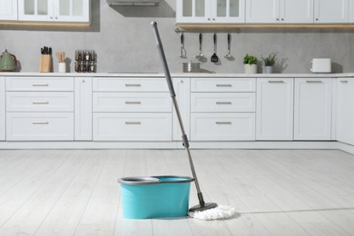 Photo of Mop and bucket on white parquet in kitchen. Cleaning floor