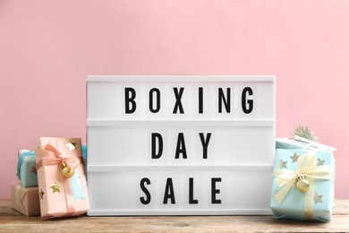 Composition with Boxing Day Sale sign and Christmas gifts on wooden table against pink background