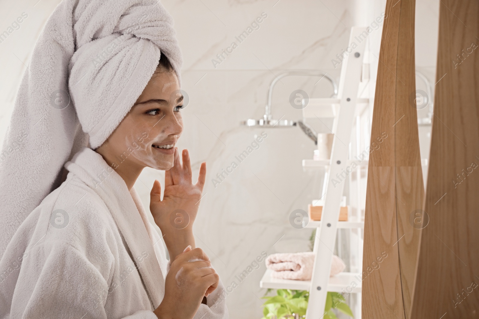 Photo of Beautiful teenage girl applying cleansing foam onto face in bathroom. Skin care cosmetic