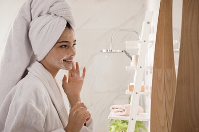 Photo of Beautiful teenage girl applying cleansing foam onto face in bathroom. Skin care cosmetic