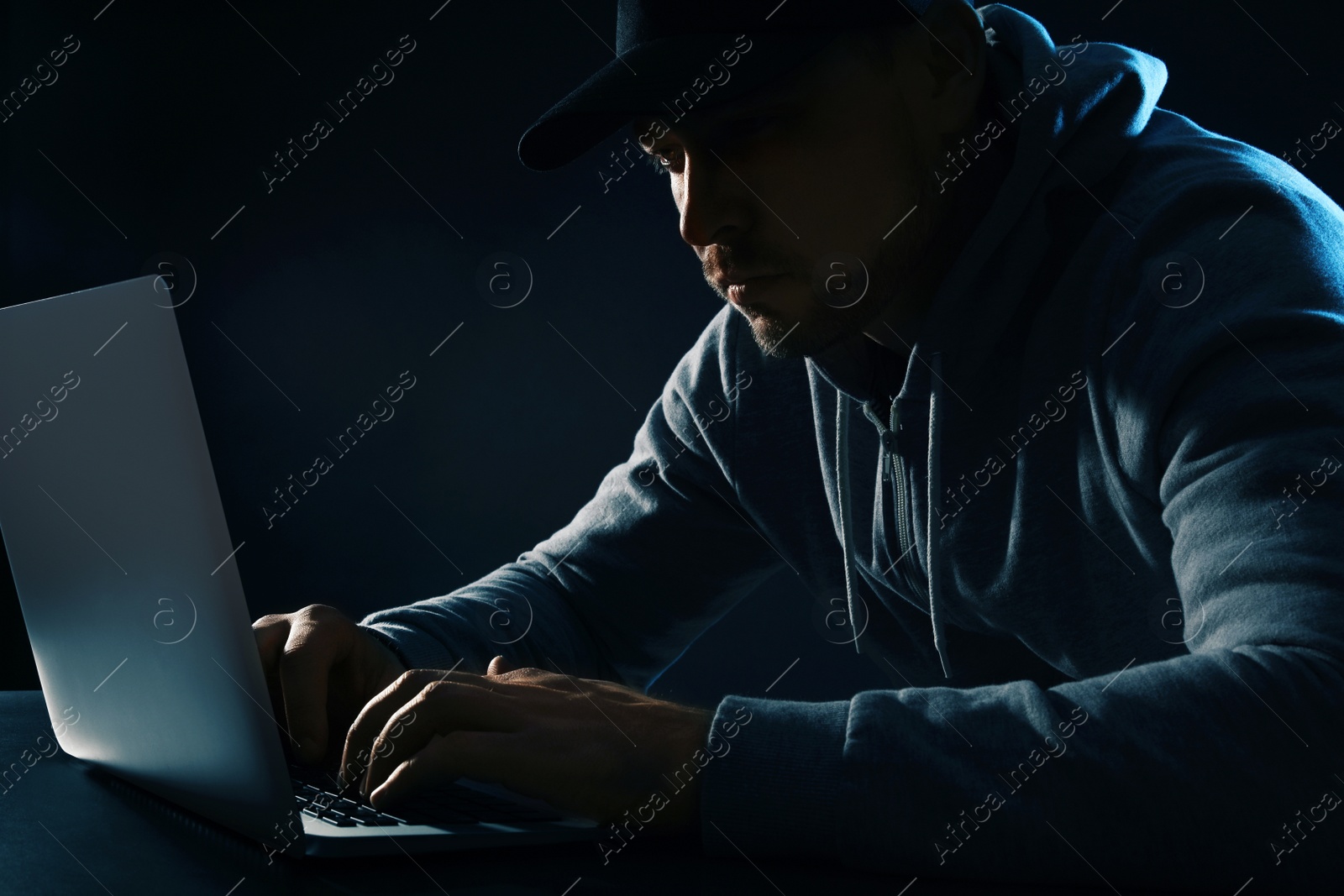 Photo of Man using laptop at table on dark background. Criminal activity