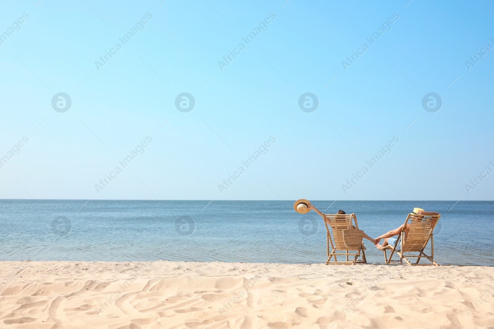 Photo of Young couple relaxing in deck chairs on beach