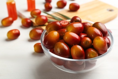 Photo of Palm oil fruits in bowl on white wooden table, closeup