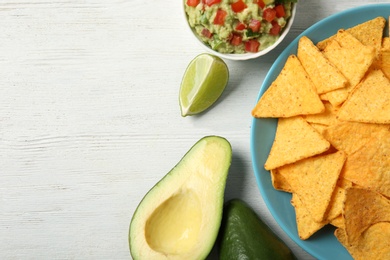 Photo of Plate with delicious mexican nachos chips, guacamole sauce, lime and avocado on white wooden table, flat lay. Space for text