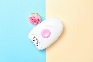 Modern epilator and flower on color background, top view