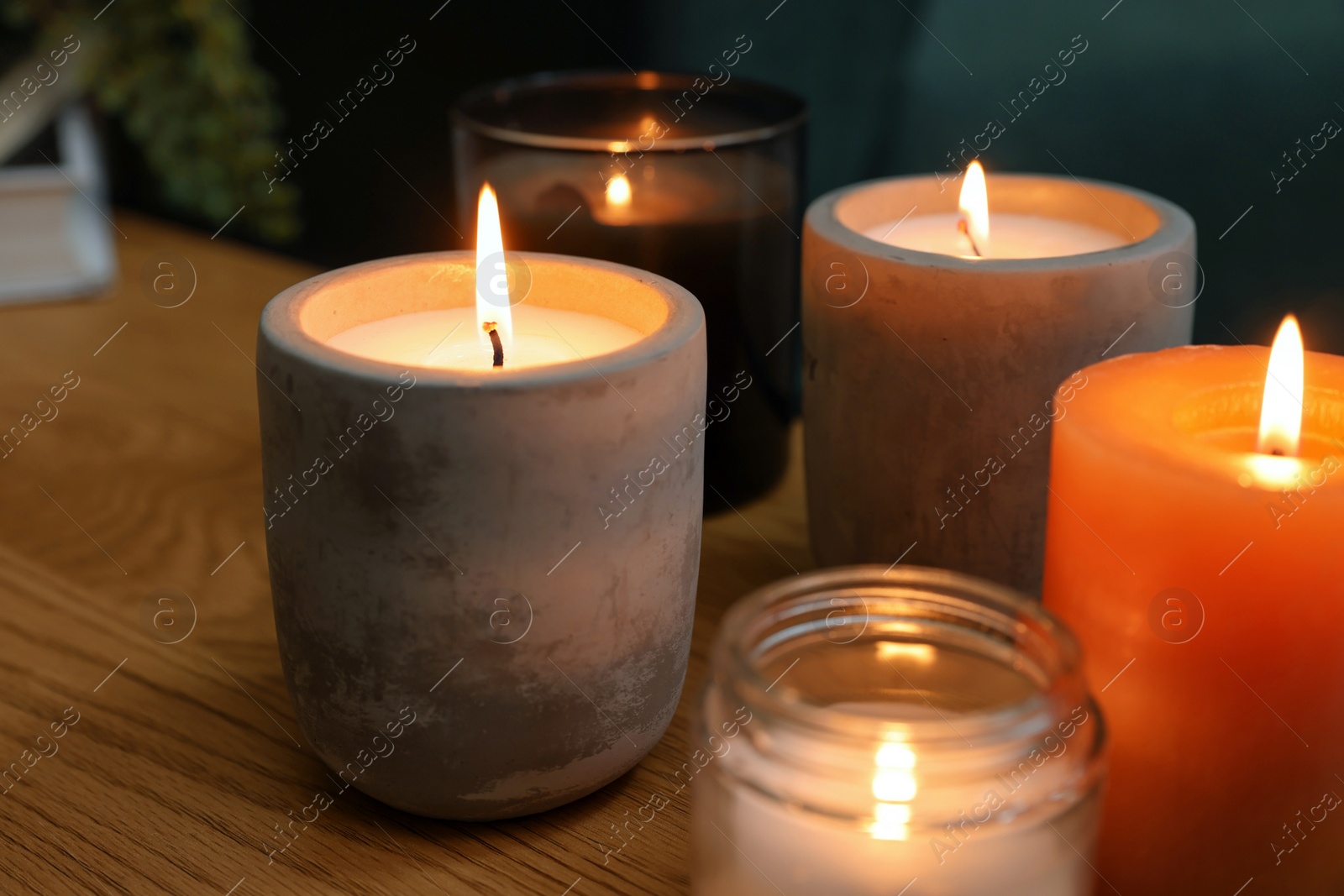 Photo of Lit candles in different holders on wooden table indoors