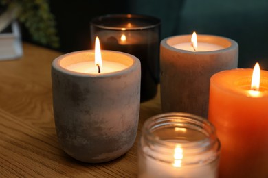 Photo of Lit candles in different holders on wooden table indoors