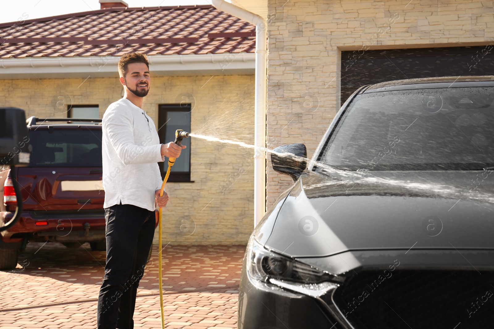 Photo of Young happy man washing car at backyard on sunny day