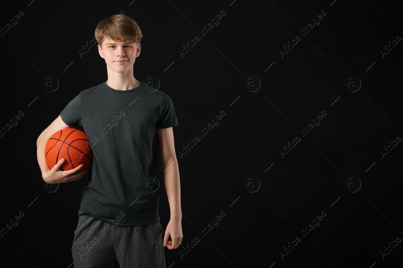 Photo of Teenage boy with basketball ball on black background. Space for text